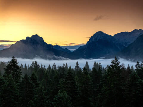 A mist-filled valley in the Dolomites at sunrise, with sunlight highlighting the peaks and dense alpine forest below. Taken near Danta village, Italy. Aerial photo with Dolomites. Hike in Italy.