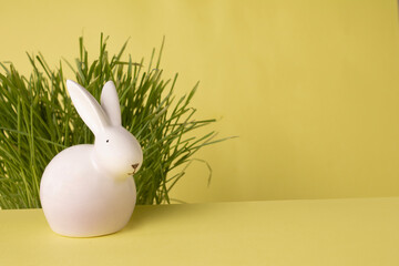 white ceramic rabbit on yellow paper background with green grass, copy space