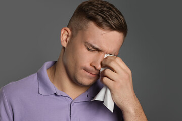 Crying man wiping tears with tissue on grey background