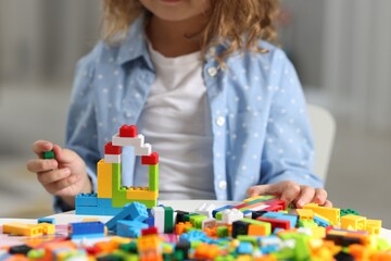 Fototapeta premium Girl playing with building blocks at white table indoors, closeup