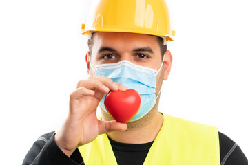 Close-up of constructor holding red heart wearing medical mask