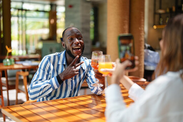 A young Black male and Caucasian female cheers with drinks at a tropical bar. The scene is set outdoors with wooden tables, creating a joyful and collaborative atmosphere for aspiring entrepreneurs.