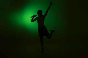 Silhouette of woman singing on dark background with green light