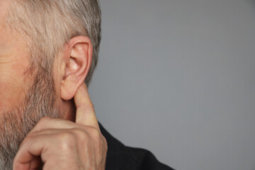 Senior man showing hand to ear gesture on grey background, closeup. Space for text