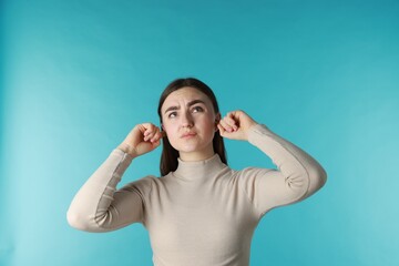 Fototapeta premium Frustrated woman covering her ears from loud noise on blue background