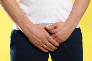 STD (sexually transmitted diseases). Man suffering from symptoms on yellow background, closeup