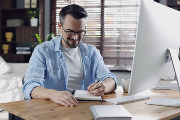 Happy man working with computer at desk indoors. Home office