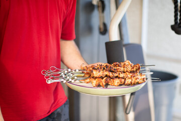 a man holding grilled chicken kebabs on a plate 