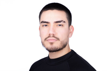 Fototapeta premium Confident serious headshot of a young man with short black hair and a beard, wearing a black high-collar shirt, set against a white background