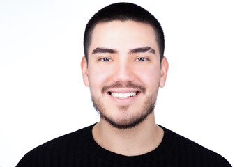 Fototapeta premium Friendly smiling portrait of a young man with short black hair and a beard, wearing a black high-collar shirt, captured against a white background