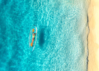 Aerial view of young woman lying on transparent canoe in blue sea at sunset. Summer in Zanzibar....