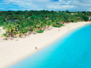Aerial view of empty white sandy beach with palms, umbrellas, blue ocean, sky with clouds at sunset. Summer in Kendwa, Zanzibar island. Tropical landscape. Clear sea with azure water. Top view