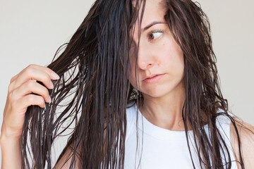 A young Caucasian brunette woman looking at her long wet tangled hair after shampooing. Hair care