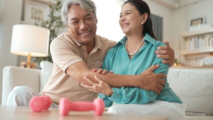 Fototapeta premium Grandmother holding dumbbell while encouraging and hugging her wife. Happy elder couple doing dumbbell exercise for enhancing flexibility or improving cardiovascular. Preventive healthcare. Myrmidon.