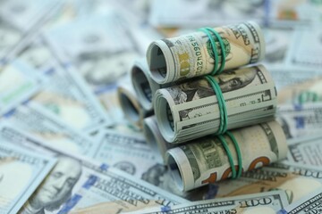 Many rolls of one hundred dollar bills lies on big amount of american currency banknotes