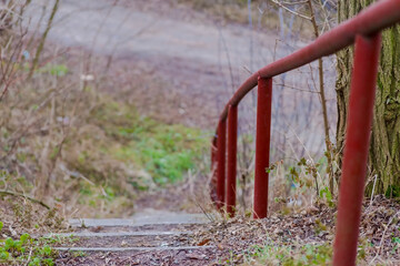 Stare betonowe schodki z czerwoną stalową poręczą. Ścieżka ( alejka) w zapomnianej części parku miejskiego na jego obrzeżach. © Grzegorz