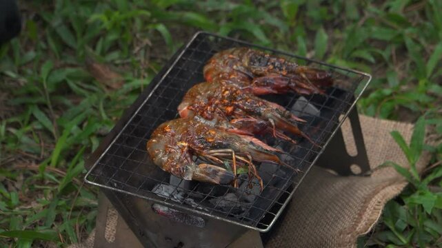 Close up of the activity of an Asian male adventurer cooking grilled shrimp using charcoal and wood. The bushcraft concept makes grilled shrimp with simple equipment in the lush wilderness