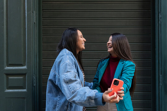 Happy latin lesbian couple laughing while holding phone