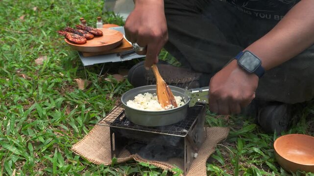 Close up of the activity of an Asian male adventurer cooking lime leaf rice using charcoal and wood. The bushcraft concept makes lime leaf rice with simple equipment in the lush wilderness
