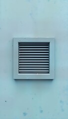 Close-up view of square metal ventilation grate set in blue wall. Fresh air circulates through metal grid. Exterior wall shows new construction. Modern ventilation system design in building. Metal