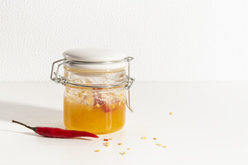 Hot honey in glass jar and red chili pepper on white background. Copy space