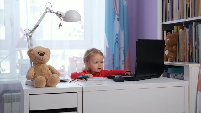 Cute baby girl sits at her workdesk, focused on a laptop and taking notes. Surrounded by teddy bears and toys. Freelance and distance work concept