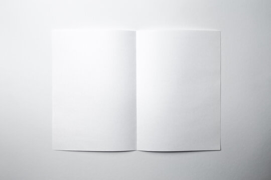 Mock up of a blank booklet with a spread on a white background. White sheet of paper with a vertical fold in the middle, with a shadow