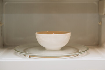 The white ceramic bowl stands on a glass base inside the microwave oven. It is perfect for demonstrating the cooking process or heating food at home..