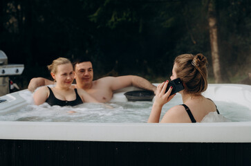 Obraz premium Three friends on a weekend in the countryside relax in a hot smart jacuzzi, enjoying the company and tranquility of the outdoors.
