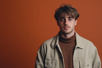 Obraz premium Stylish Young Man Posing Against a Warm Orange Background in Casual Fashion