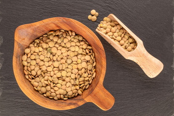 Lentil seeds in a wooden cup with a wooden spoon on a slate stone, close-up, top view.
