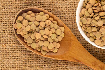 Lentil seeds in a ceramic plate with a wooden spoon on a jute cloth, macro, top view.