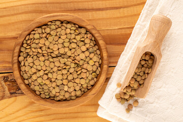 Lentil seeds in a wooden plate with a wooden spoon on a wooden table, close-up, top view.