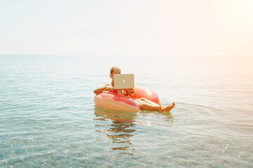 Woman laptop sea. Freelancer woman in sunglases floating on an inflatable big pink donut with a laptop in the sea. People summer vacation rest lifestyle concept