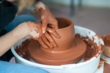 Female hands throwing a large sized bowl on a potter's wheel in a sunlit pottery studio
