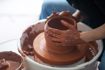 Female hands throwing a large sized bowl on a potter's wheel in a sunlit pottery studio