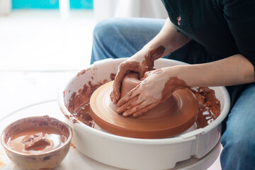 Female hands throwing a large sized bowl on a potter's wheel in a sunlit pottery studio