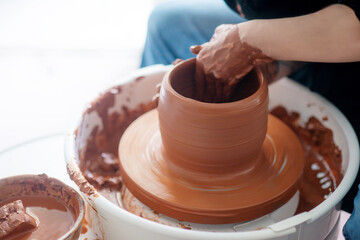 Female hands throwing a large sized bowl on a potter's wheel in a sunlit pottery studio