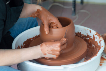 Female hands throwing a large sized bowl on a potter's wheel in a sunlit pottery studio