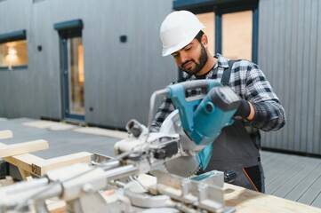 Indian carpenter cuts a wooden plank on a sawmill in a modular building factory, providing precise...