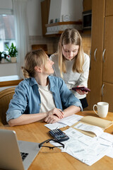 Mom and daughter look at bills and papers together at the table, discussing financial issues. The...