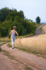 Obraz premium A teenager running down a winding field road going off into the horizon.