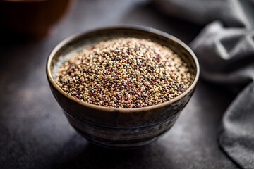 Mixed uncooked quinoa seeds in bowl on black table.