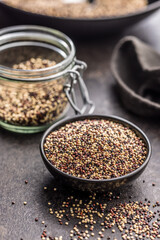 Mixed uncooked quinoa seeds in bowl on black table.