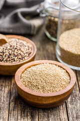 Mixed uncooked quinoa seeds in bowl on wooden table.