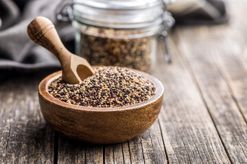 Mixed uncooked quinoa seeds in bowl on wooden table.