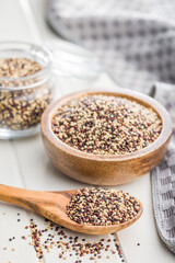 Mixed uncooked quinoa seeds on wooden spoon on white table.