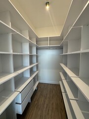 Obraz premium Spacious walk-in closet with white shelving and modern wooden flooring