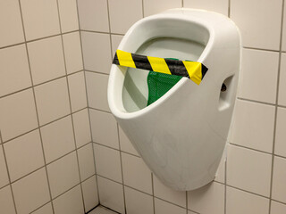 Broken urinal taped with yellow and black tape in a public restroom