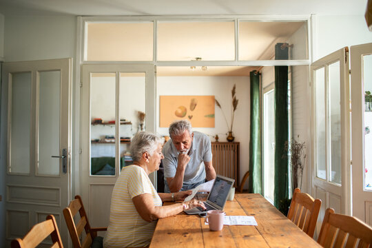 Senior couple doing bills with laptop on the kitchen table